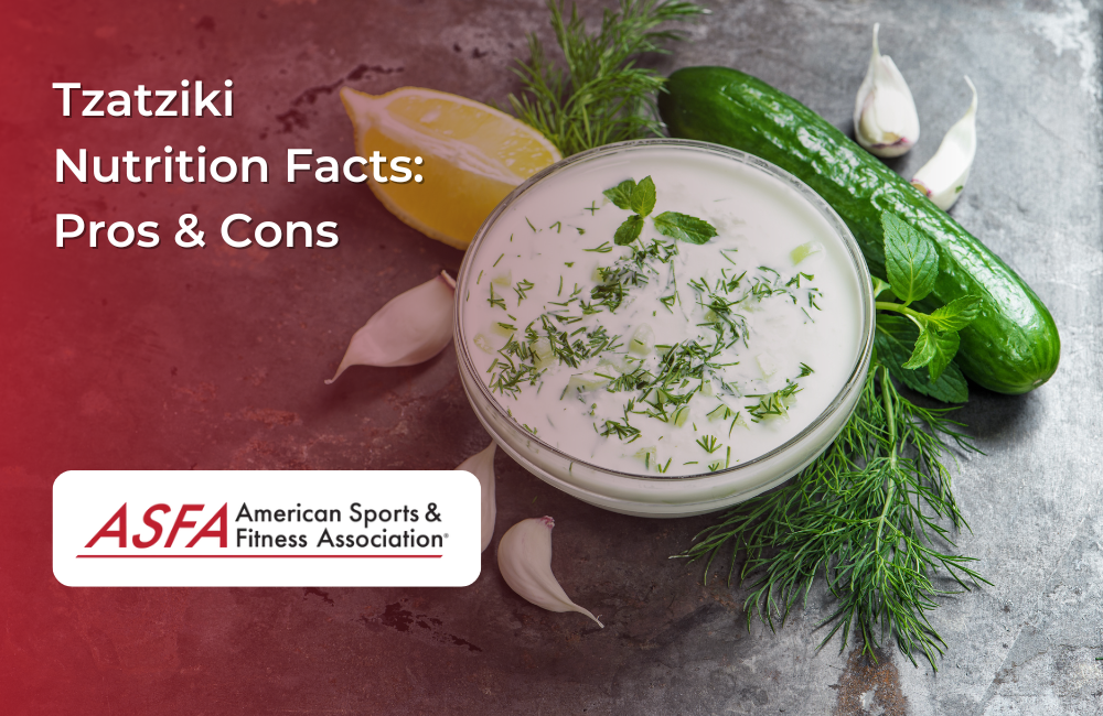 A bowl of creamy tzatziki sauce garnished with dill, surrounded by cucumbers, garlic, lemon, and fresh herbs.
