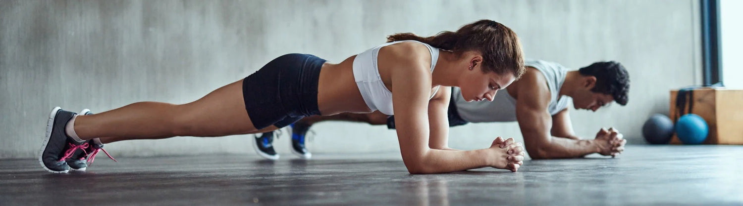 Woman in foreground and man in background in gym performing a plank