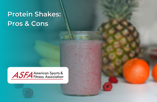 Protein shake in a glass jar with various fruits in background, such as an orange, pineapple, a bunch of bananas, and raspberries.