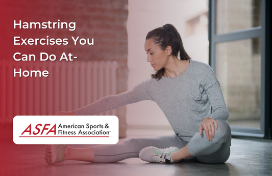 A woman in a gray long-sleeve shirt and leggings sitting on the floor indoors, stretching one leg while reaching for her foot. A radiator and window are visible in the background.