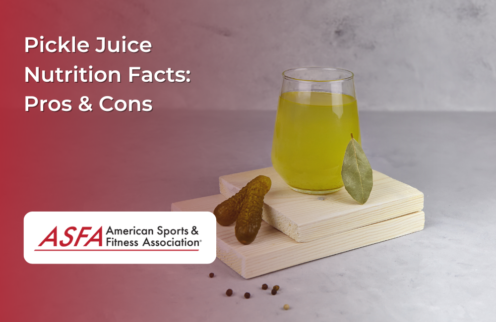 A glass of bright yellow-green pickle juice with a pickle and bay leaf on a small wooden board.