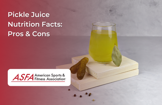 A glass of bright yellow-green pickle juice with a pickle and bay leaf on a small wooden board.