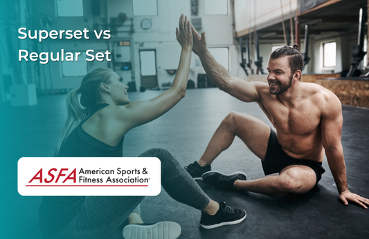 A man and woman in workout attire smile and high-five while sitting on a gym floor.