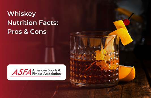 A glass of whiskey garnished with an orange peel and cherry sits on a wooden surface.