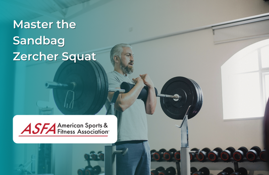 Older man performing a Zercher squat with a barbell indoors near weight racks.