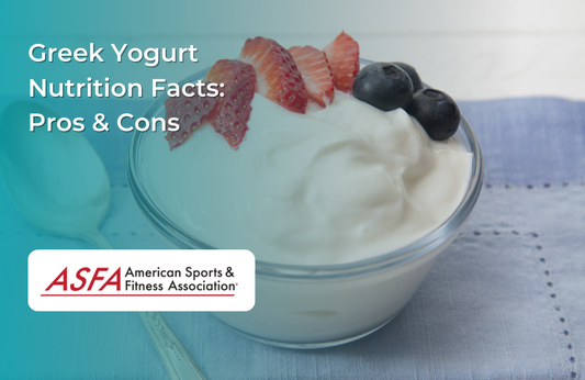 A glass bowl filled with Greek yogurt topped with strawberries and blueberries on a blue cloth.