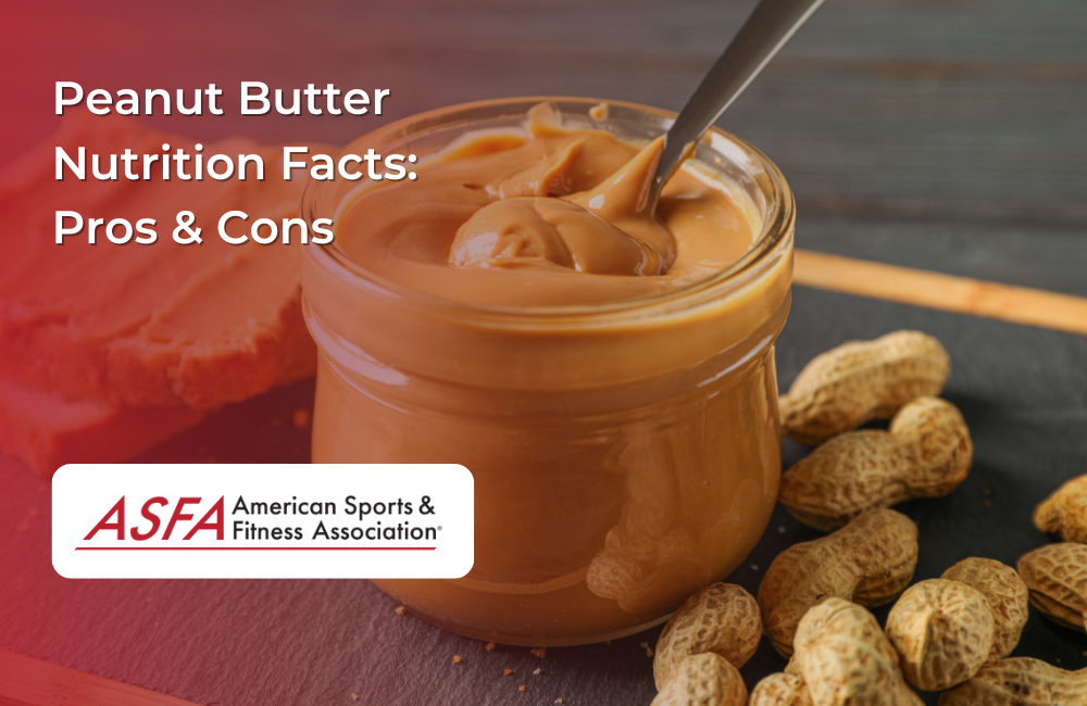 A jar of creamy peanut butter with a spoon inside, surrounded by whole peanuts on a wooden table.