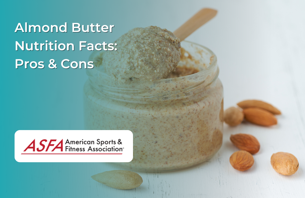 A jar of almond butter with a wooden spoon scooping it out, accompanied by scattered almonds on a white surface.