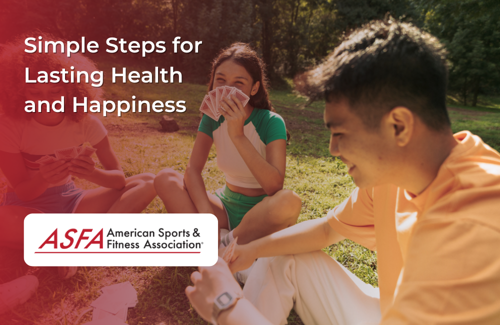 Three people sit on the grass in a sunny park laughing and playing cards together.