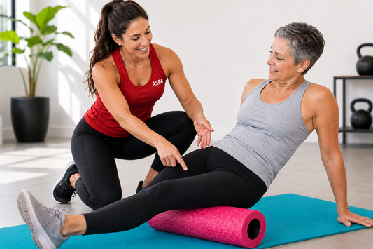 ASFA foam rolling instructor guiding an older client using a hot pink foam roller on a teal exercise mat
