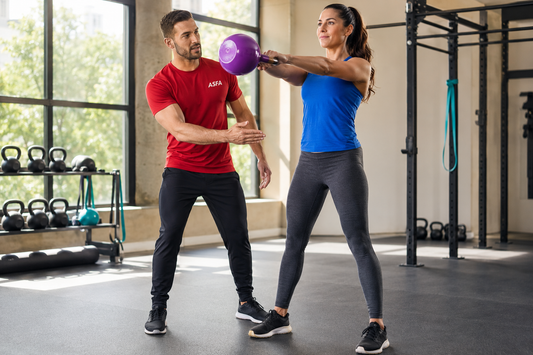ASFA kettlebell trainer coaching a woman through a two-handed kettlebell swing in a bright gym
